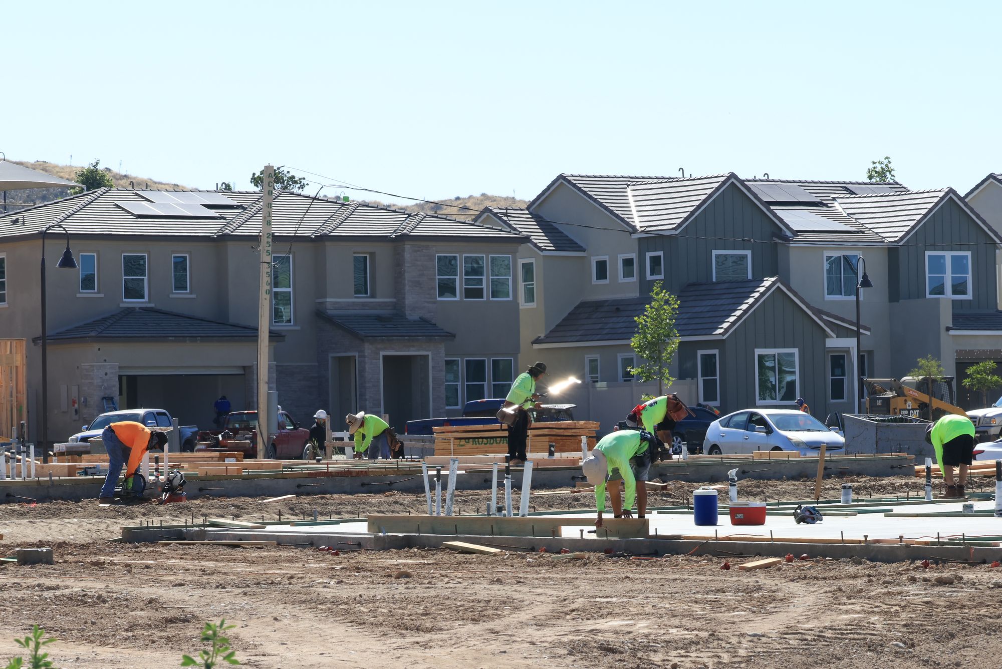 Crew setting footing forms and rebar for a new home foundation with a skid steer nearby